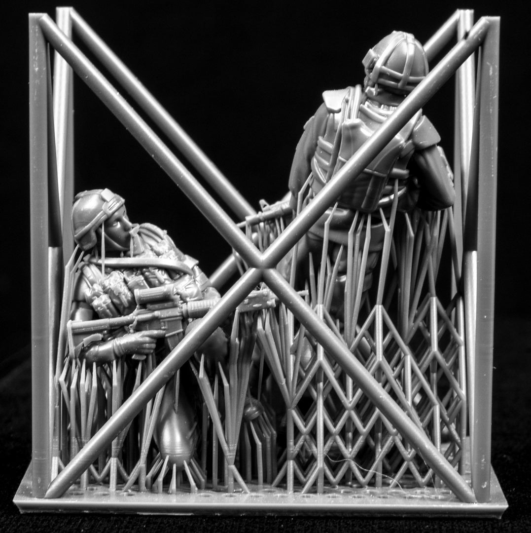 Two miniature figures in tactical gear behind a metal barrier on a black background