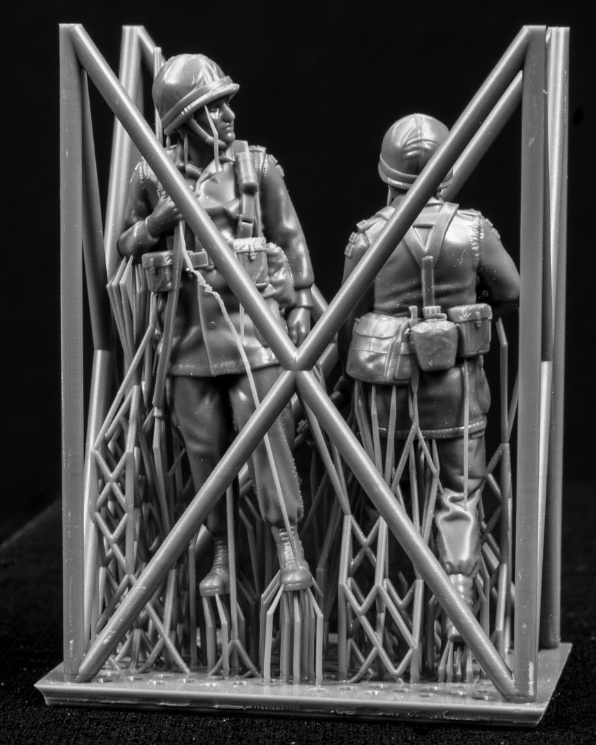 Two miniature figures of soldiers with gear inside a frame on a black background