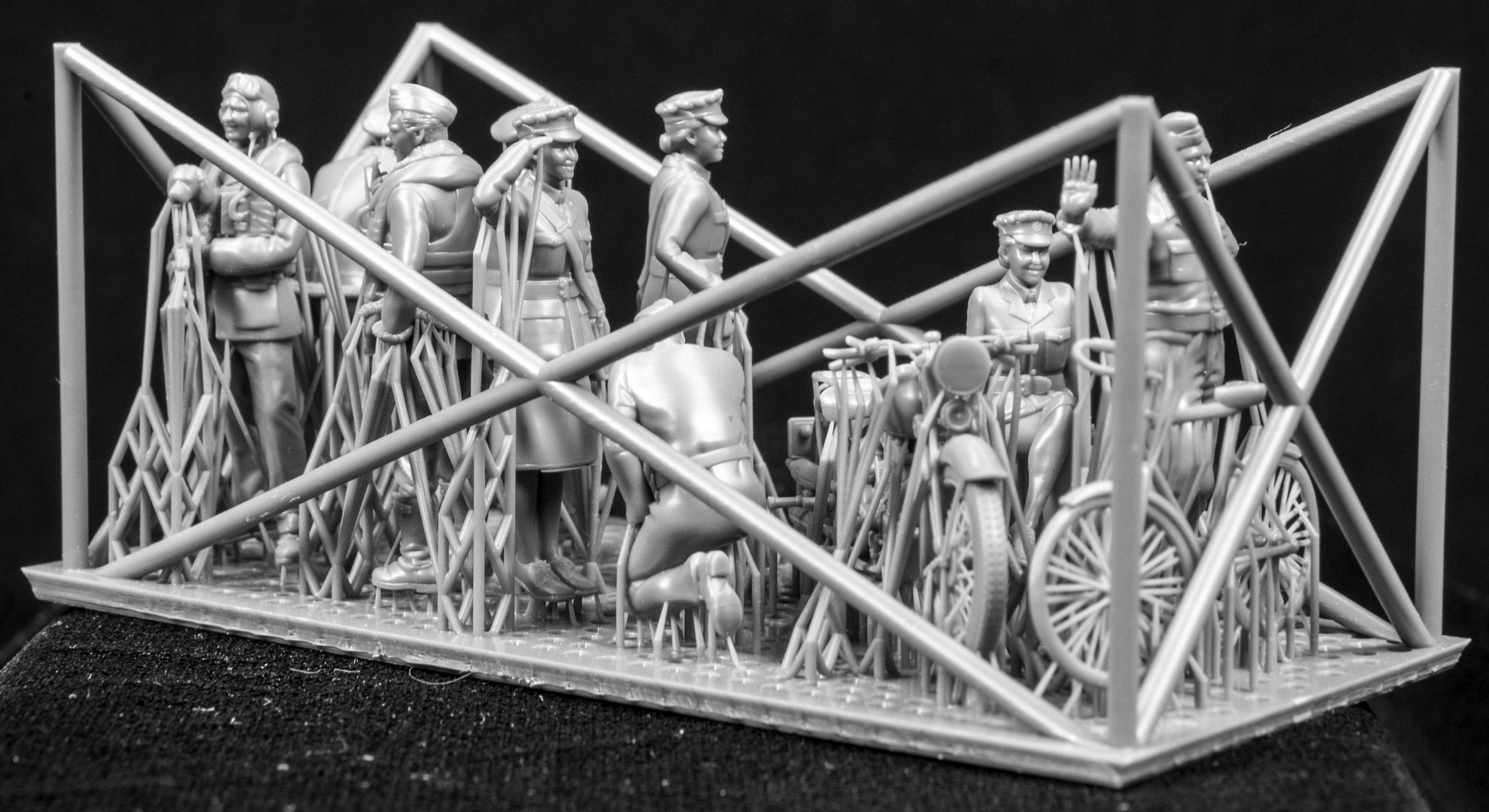 A collection of 3D printed figures, motorcycle and bicycle on a frame with a black background.
