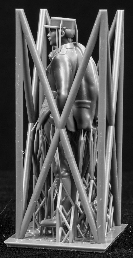 Model figure of a pilot behind a protective grid on a black background
