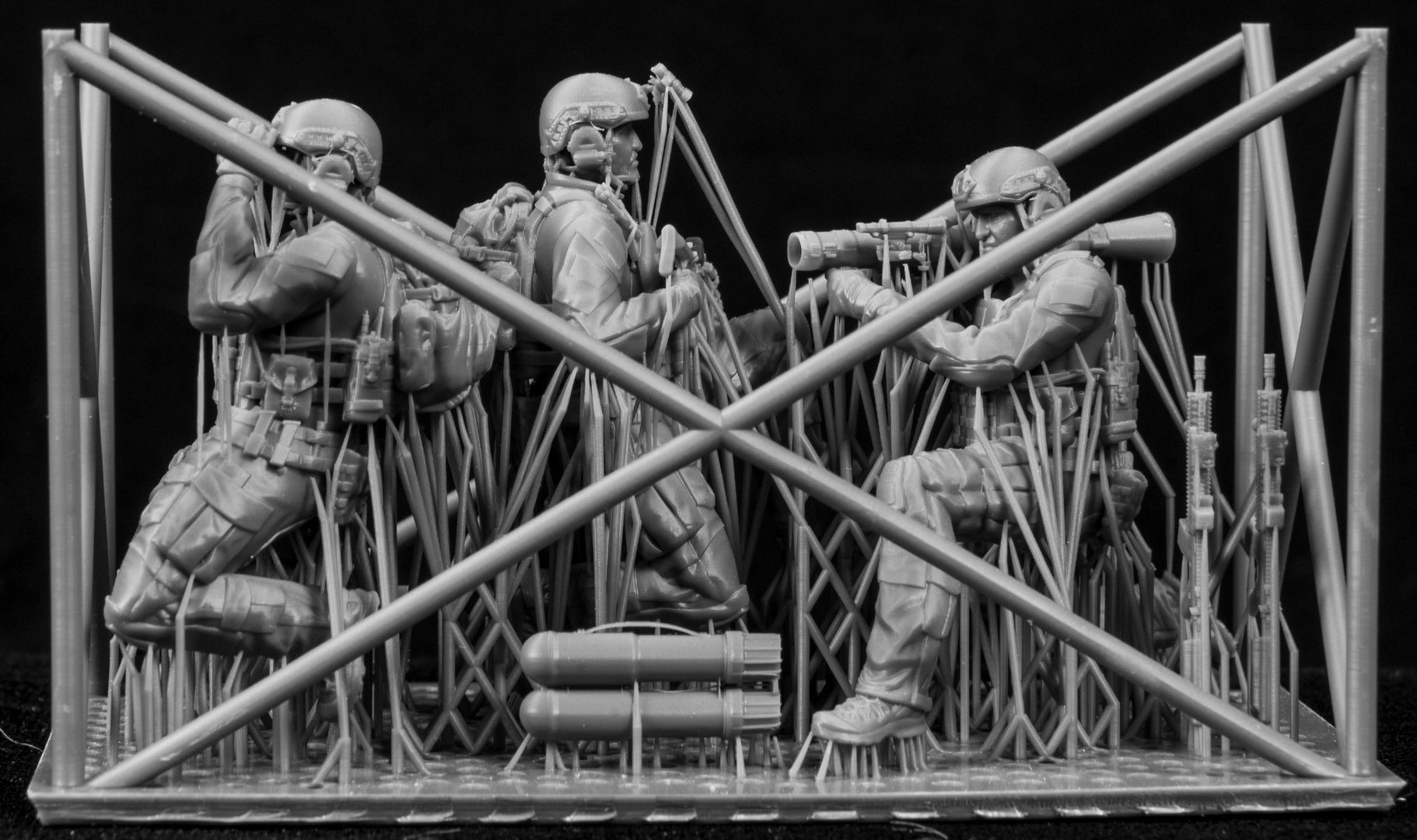 Black and white model of three soldiers with weapons and equipment on a stand.